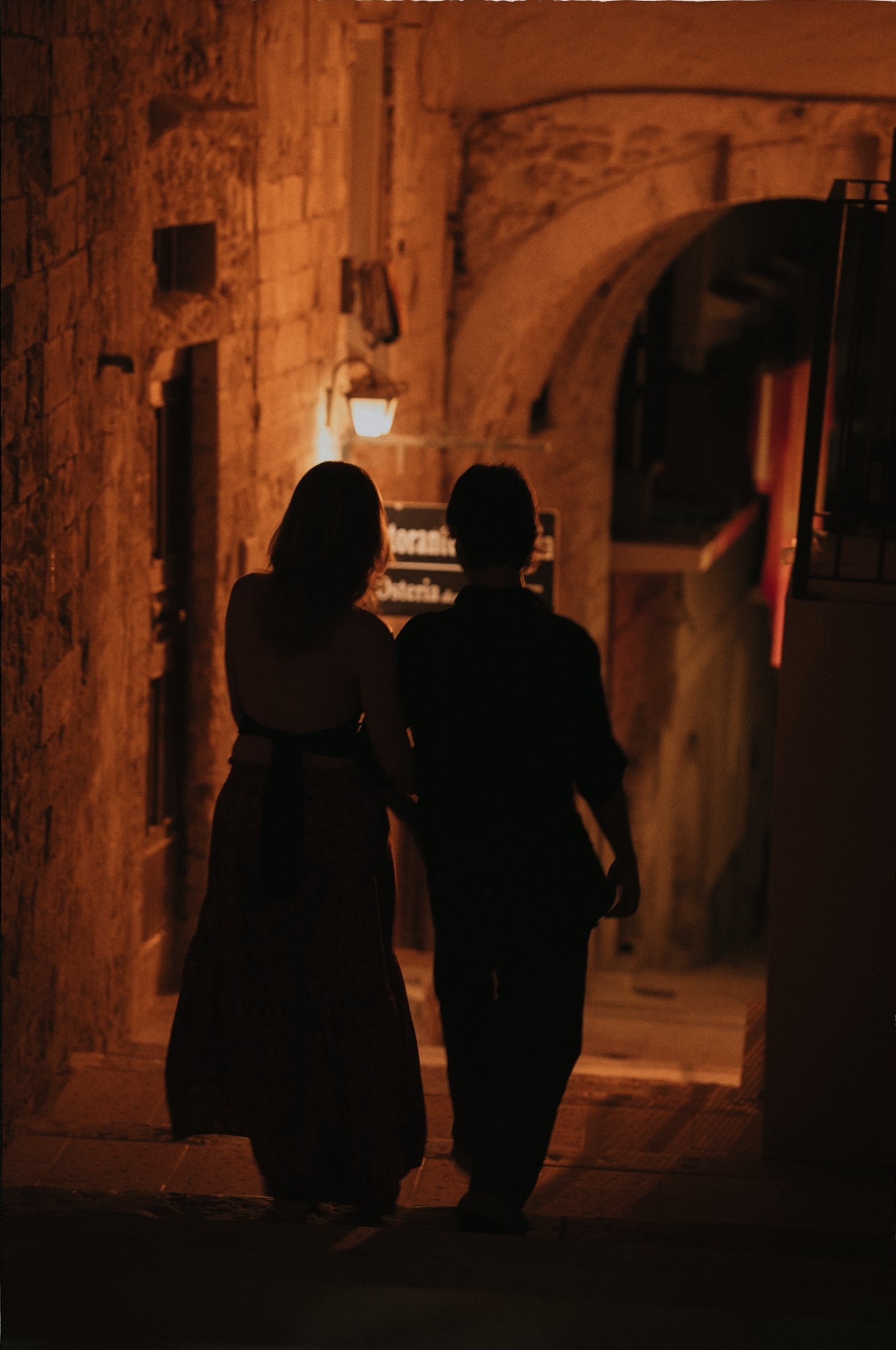 A couple silhouetted in a warm-lit stone alley at night