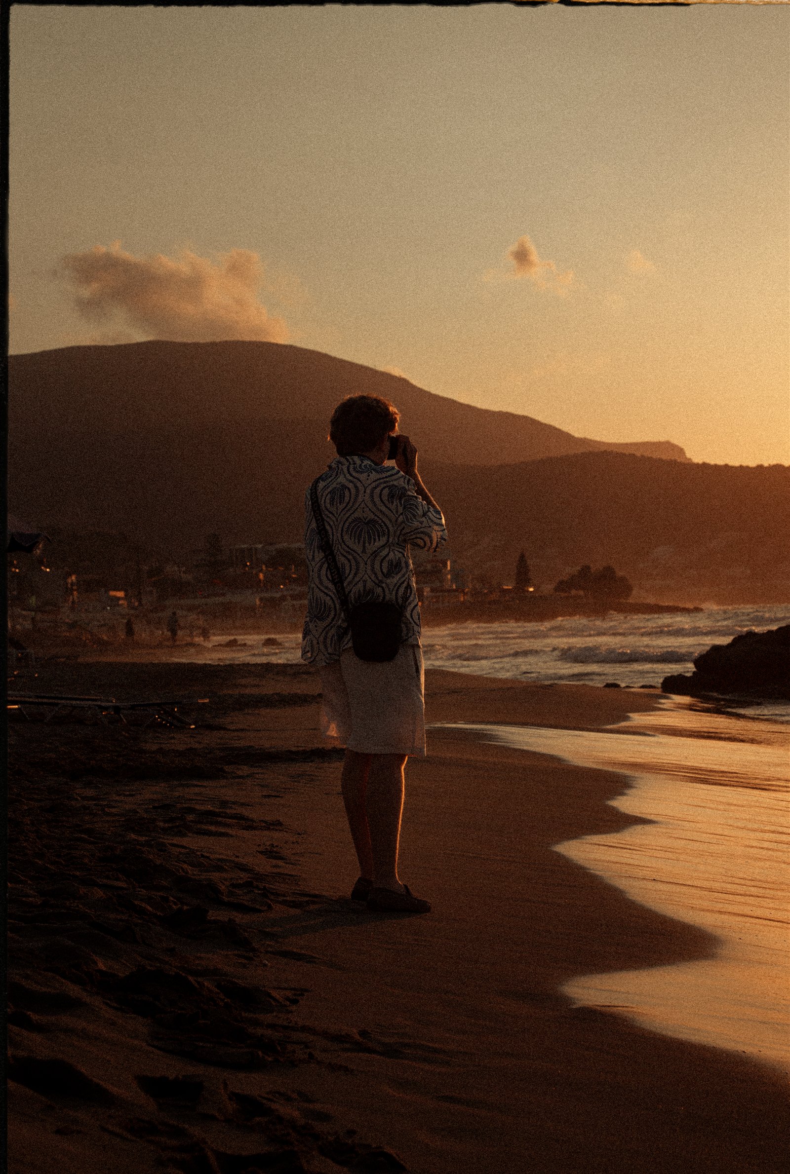 A person photographing the sunset on a beach at golden hour